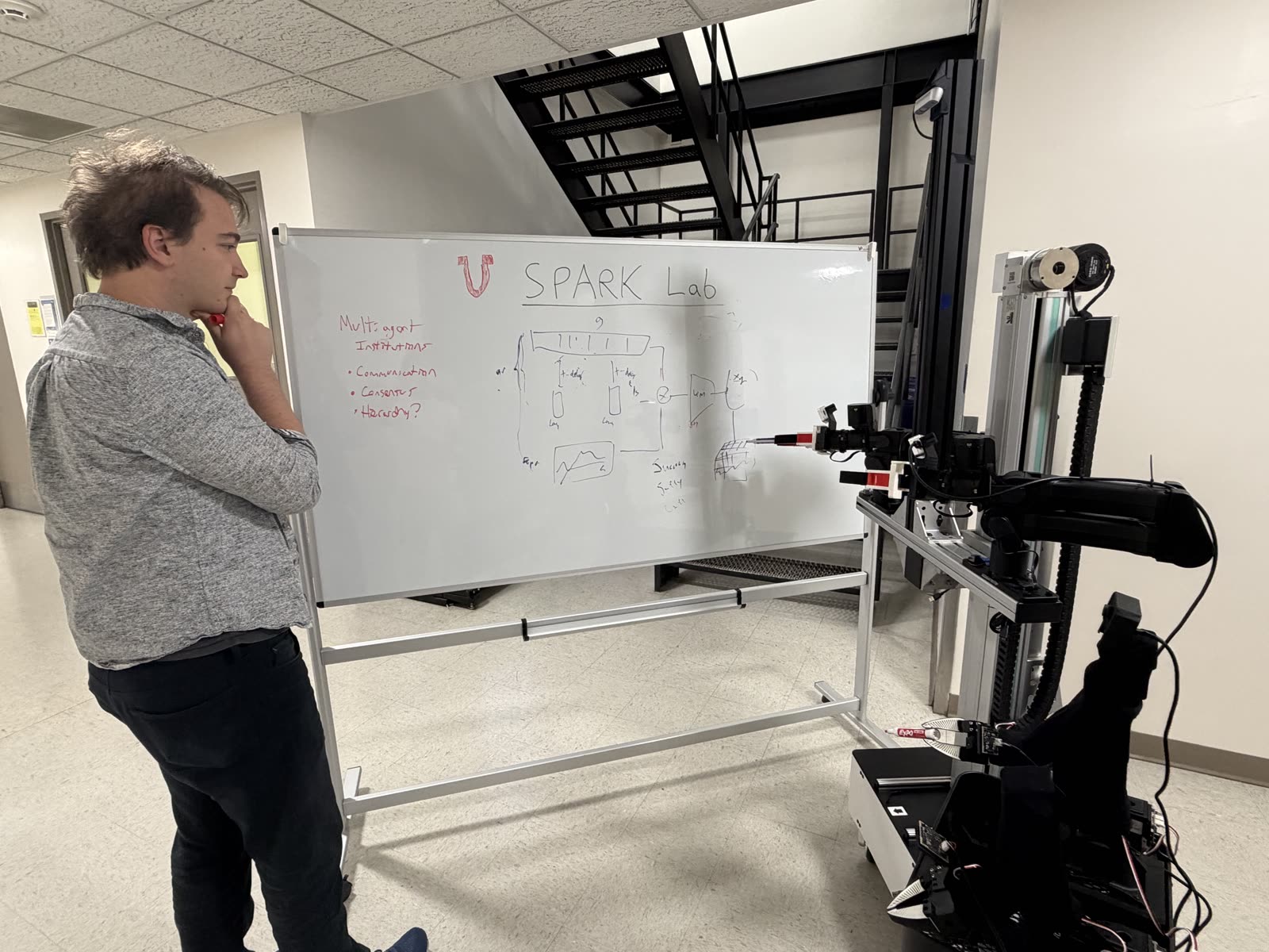 Prof. Kenneth Marino at a whiteboard sketching a SPARK Lab architecture next to a mobile robot